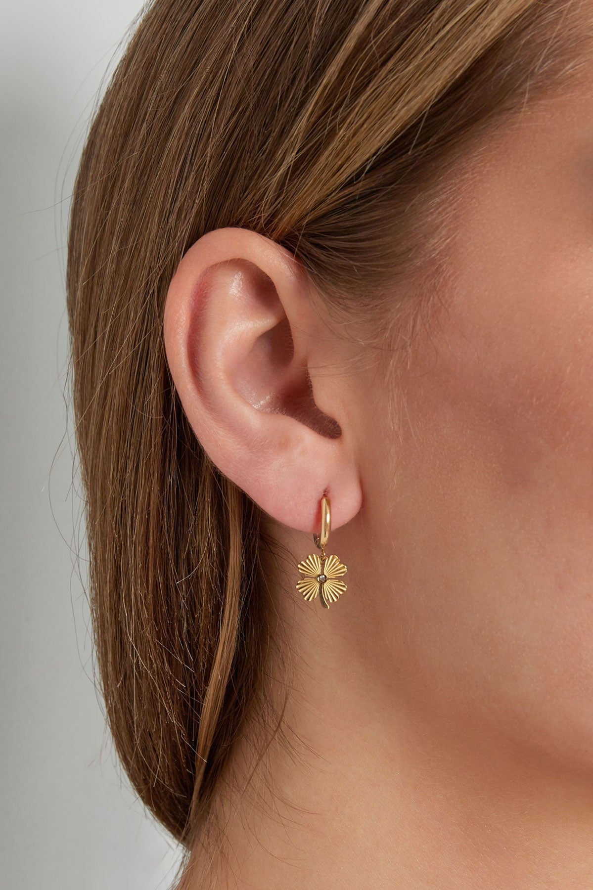 Model wearing gold-tone hoop earring with small four-leaf clover charm on ear, showcasing size and fit