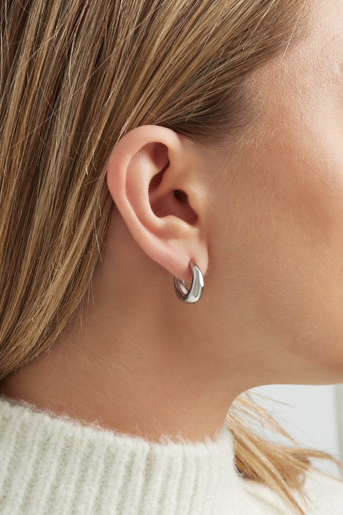 Close-up view of silver chunky hoop earring worn on a woman's ear showcasing minimalist design