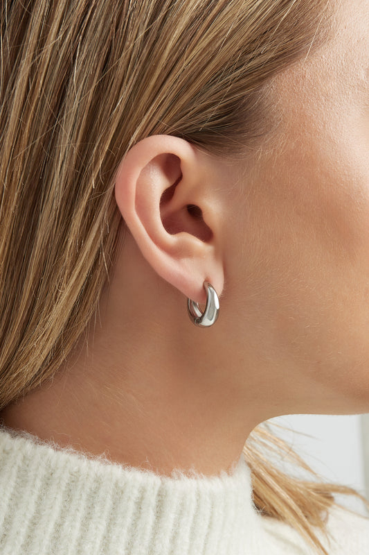 Close-up view of silver chunky hoop earring worn on a woman's ear showcasing minimalist design