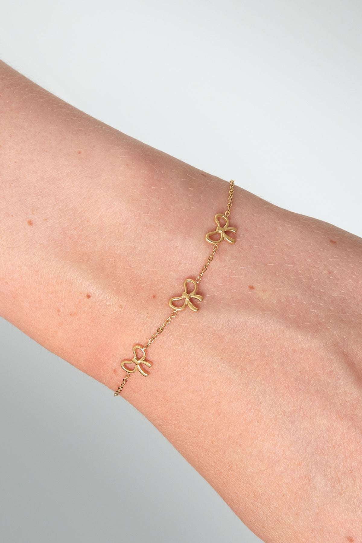 Close-up of gold bow charm bracelet worn on wrist showing fine chain and three dainty bows