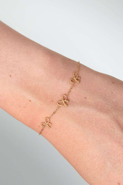 Close-up of gold bow charm bracelet worn on wrist showing fine chain and three dainty bows