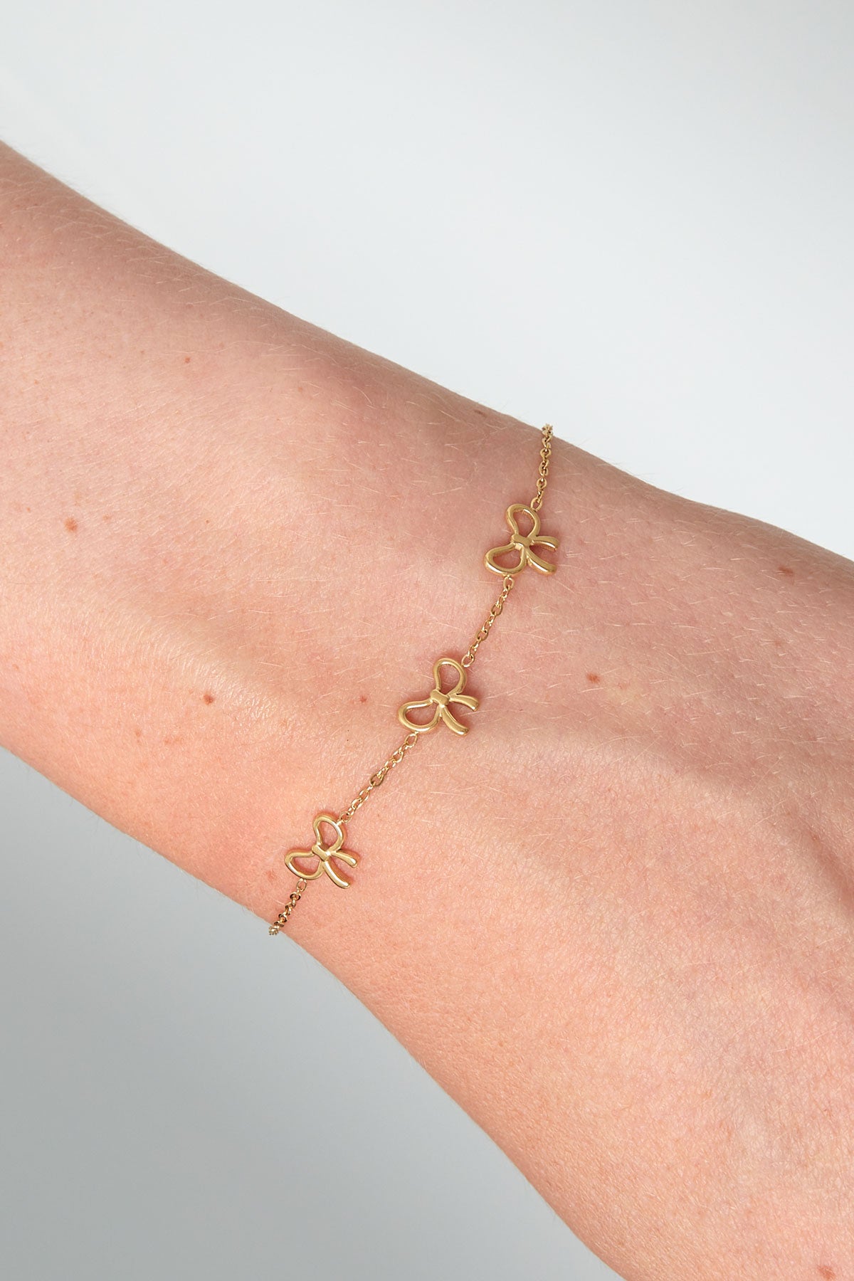 Close-up of gold bow charm bracelet worn on wrist showing fine chain and three dainty bows