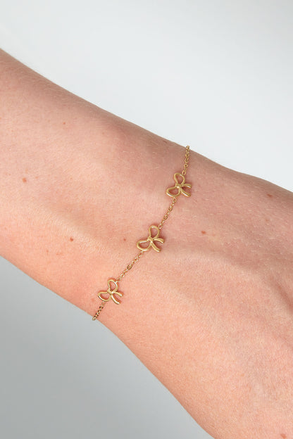 Close-up of gold bow charm bracelet worn on wrist showing fine chain and three dainty bows