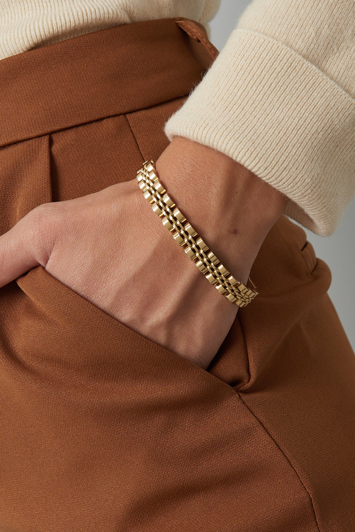 Close-up of gold double-row link chain bracelet on woman's wrist with beige sweater and brown pants