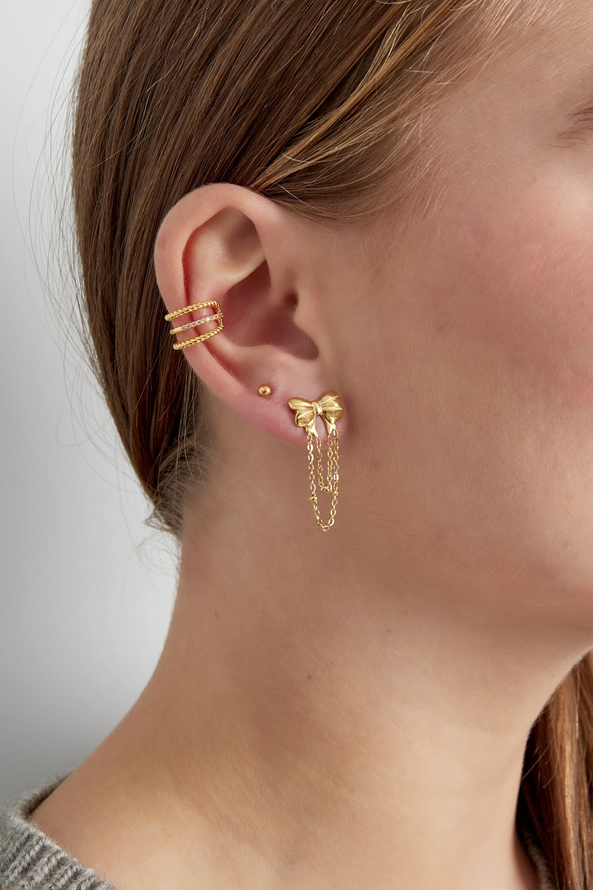 Woman wearing gold-tone ear cuff along with other gold earrings including a bow and chains