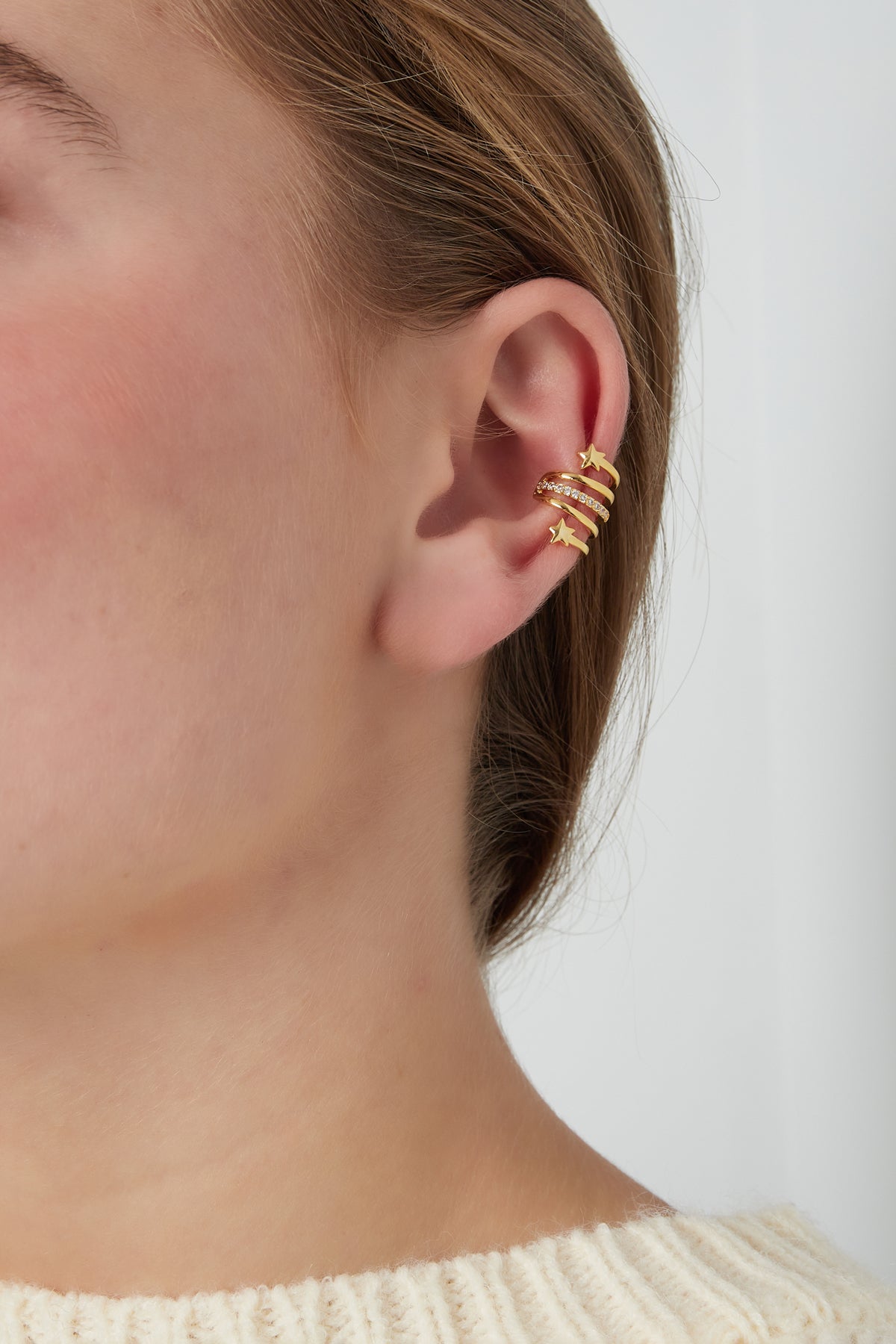 Close-up of gold-tone spiral star ear cuff worn on upper ear of a woman