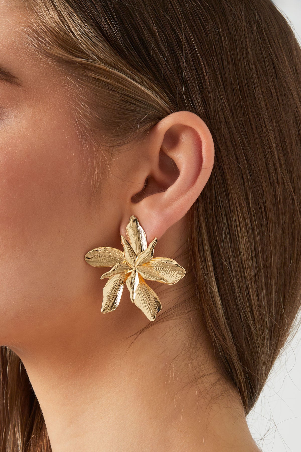 Model wearing a gold flower stud earring showcasing size and youthful, aesthetic appeal