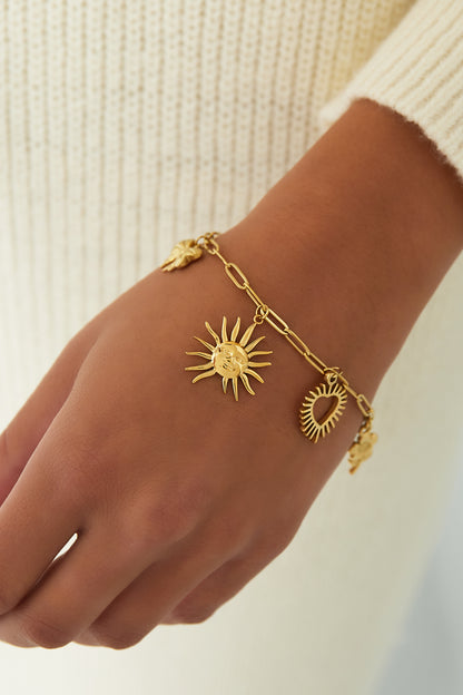 Close-up of gold-tone charm bracelet worn on wrist against soft cream sweater