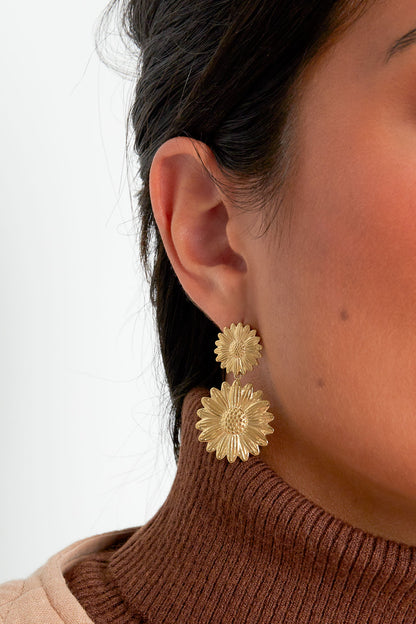 Close-up of model wearing gold sunflower drop earrings paired with brown turtleneck sweater