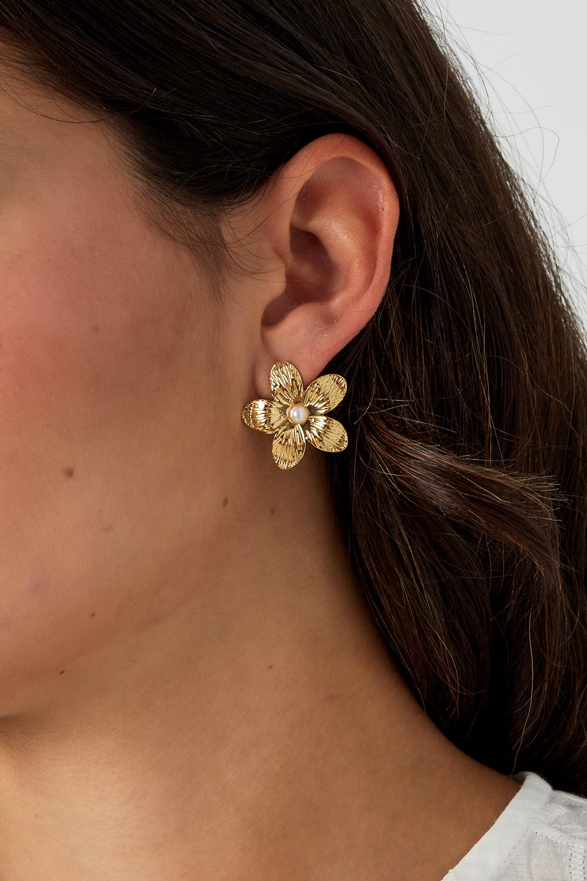 Close-up of a woman wearing gold-tone floral pearl stud earring, showing size and style against her ear