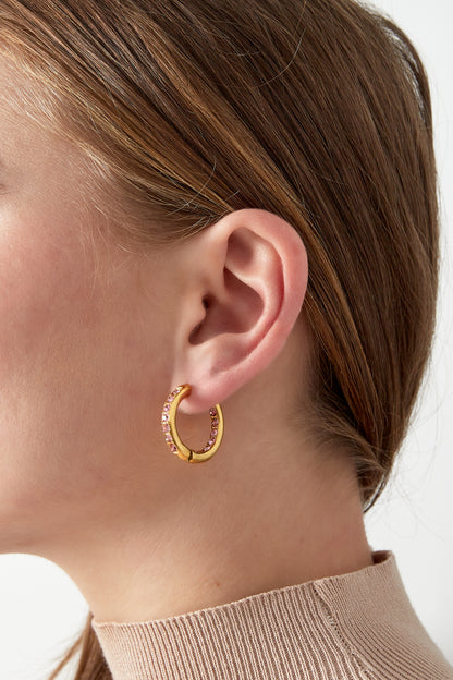 Close-up of a woman wearing gold hoop earrings with pink rhinestones, showing the comfortable fit