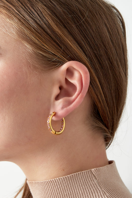 Close-up of a woman wearing gold hoop earrings with pink rhinestones, showing the comfortable fit