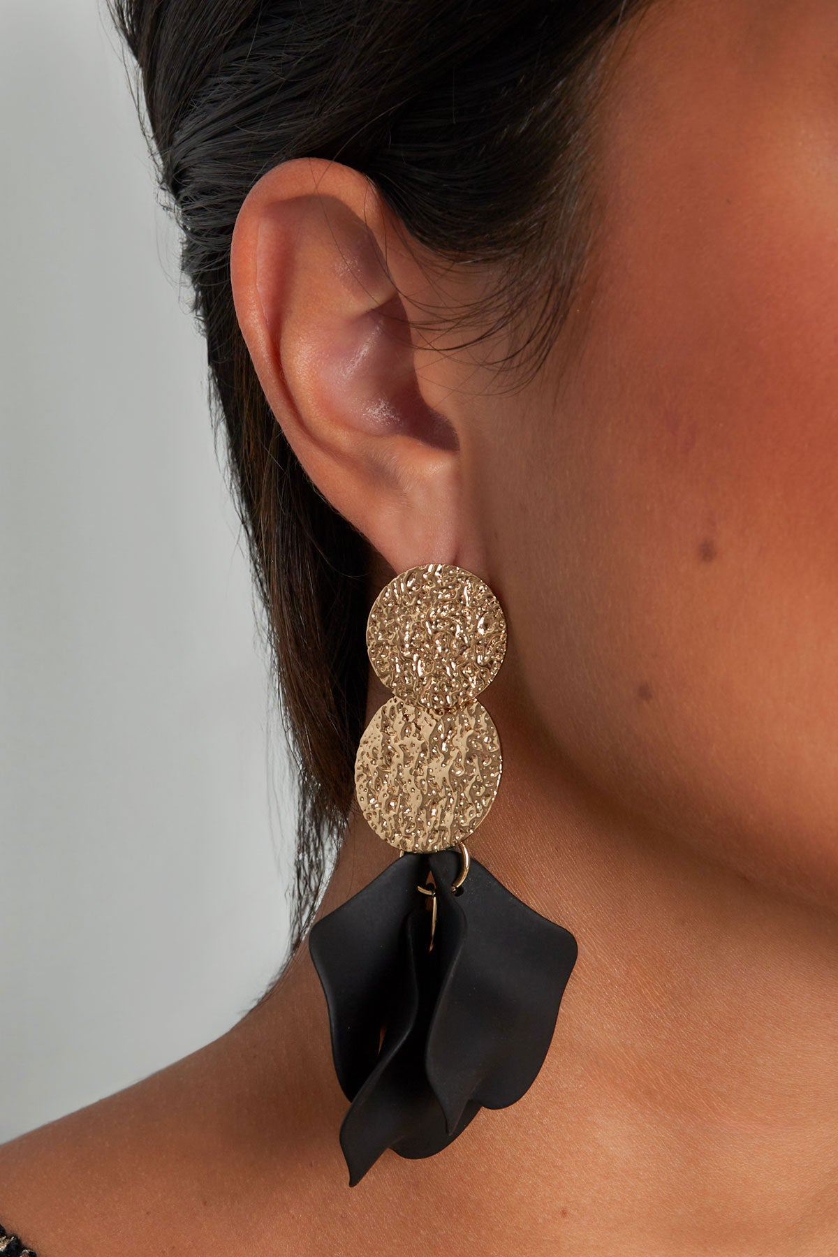 Model wearing textured gold disc earrings with black soft petal drops