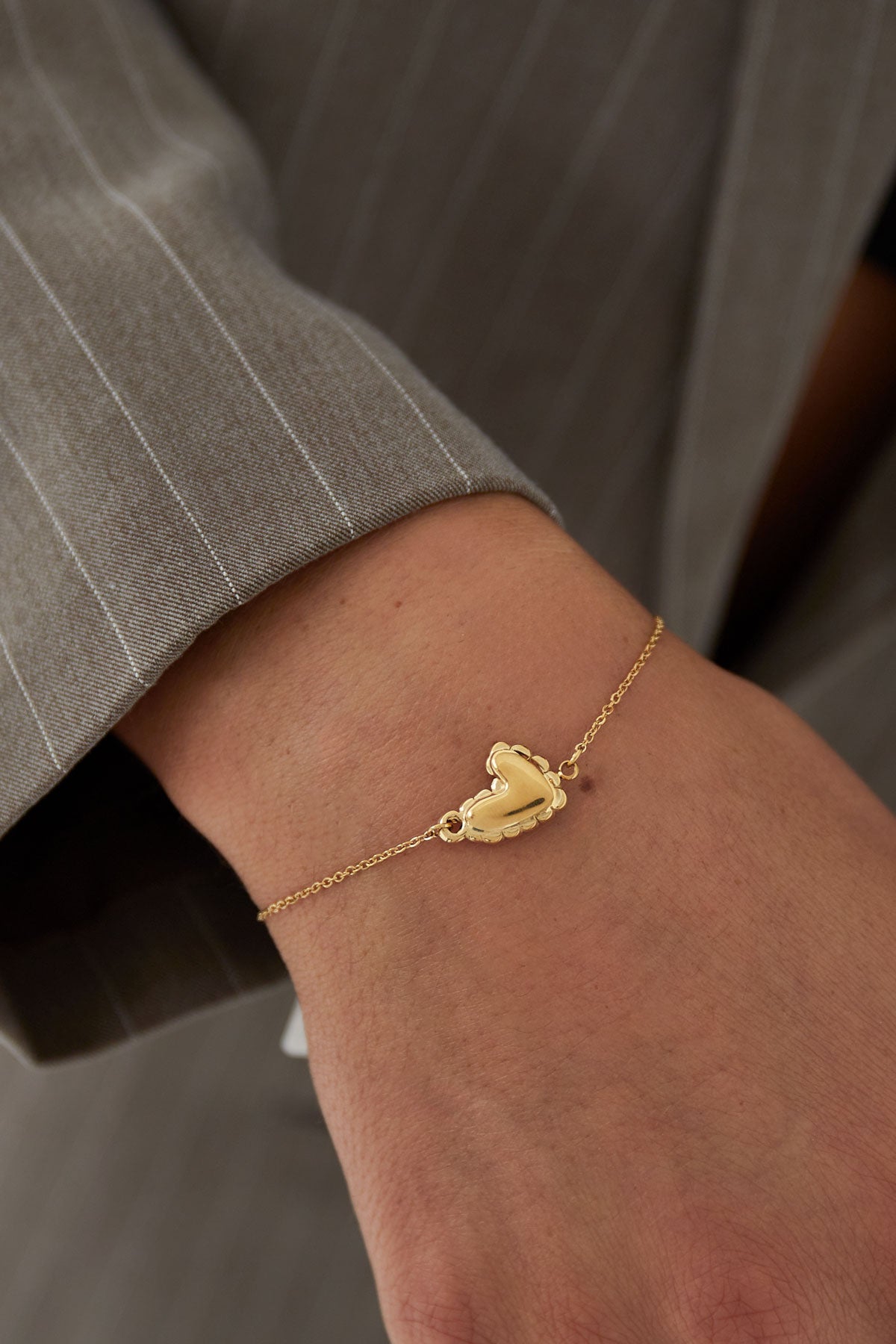 Close-up of gold heart bracelet worn on wrist with grey pinstripe sleeve visible