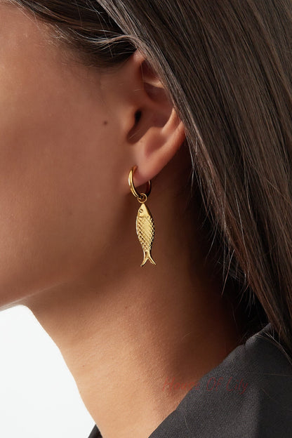Close-up of a woman wearing a gold fish charm drop earring, showing the pendant detail and hoop
