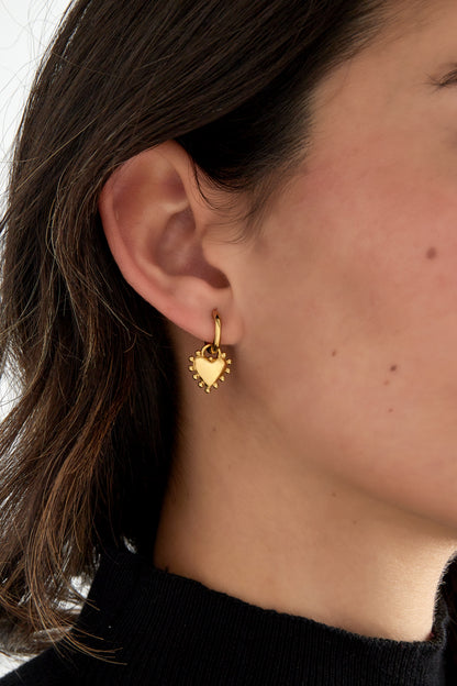 Close-up of gold heart charm hoop earring worn by woman with dark hair