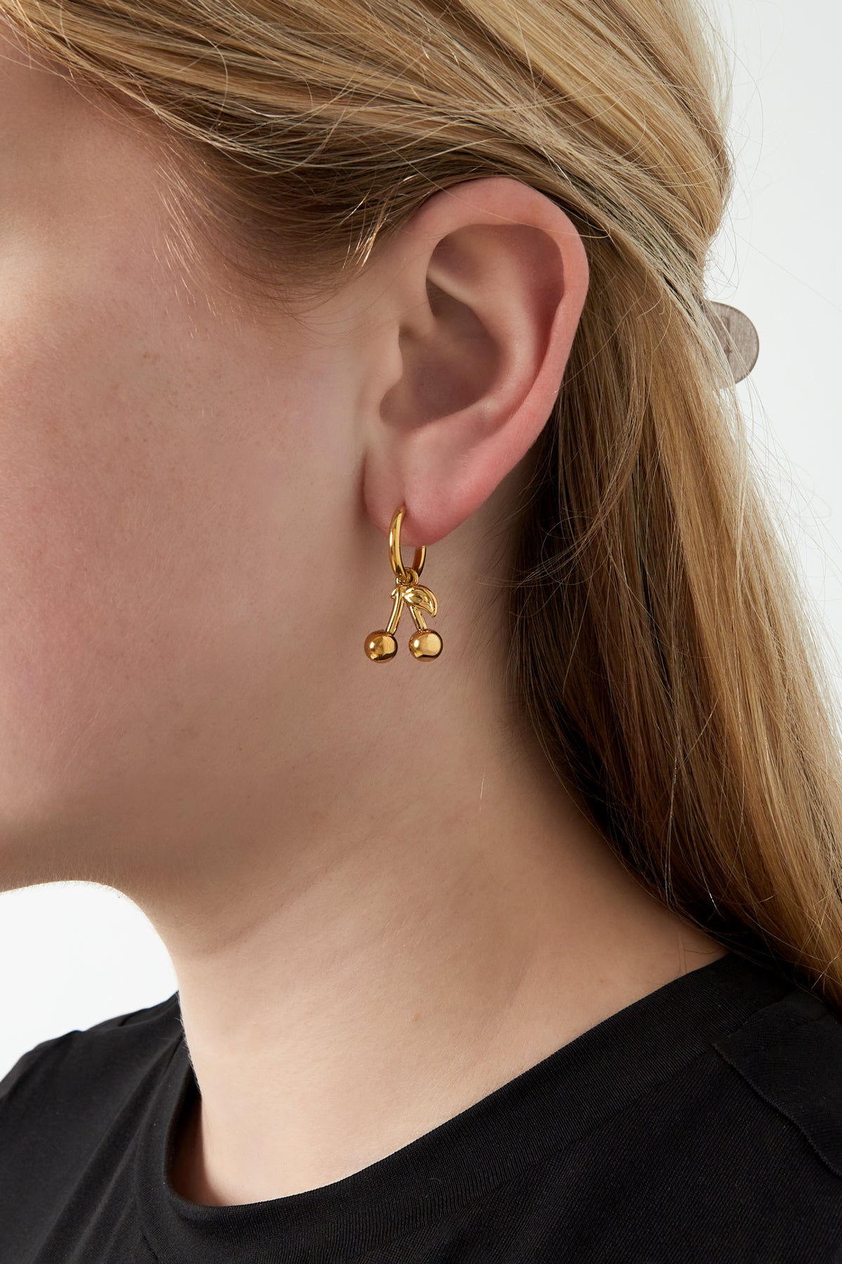 Close-up of a woman wearing gold cherry hoop earrings showcasing the playful, youthful design