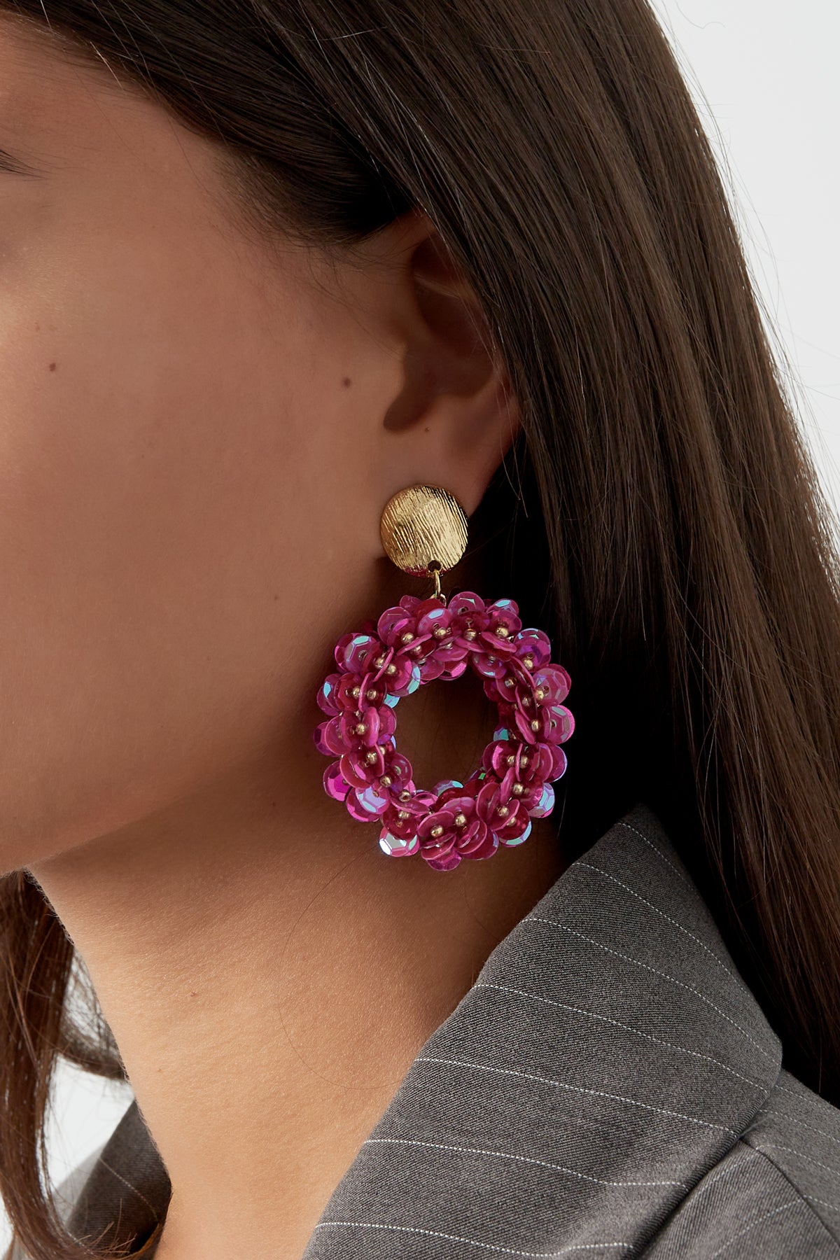 Close-up of woman wearing vibrant fuchsia sequin hoop earrings with gold textured studs