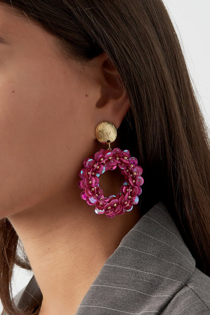 Close-up of woman wearing vibrant fuchsia sequin hoop earrings with gold textured studs