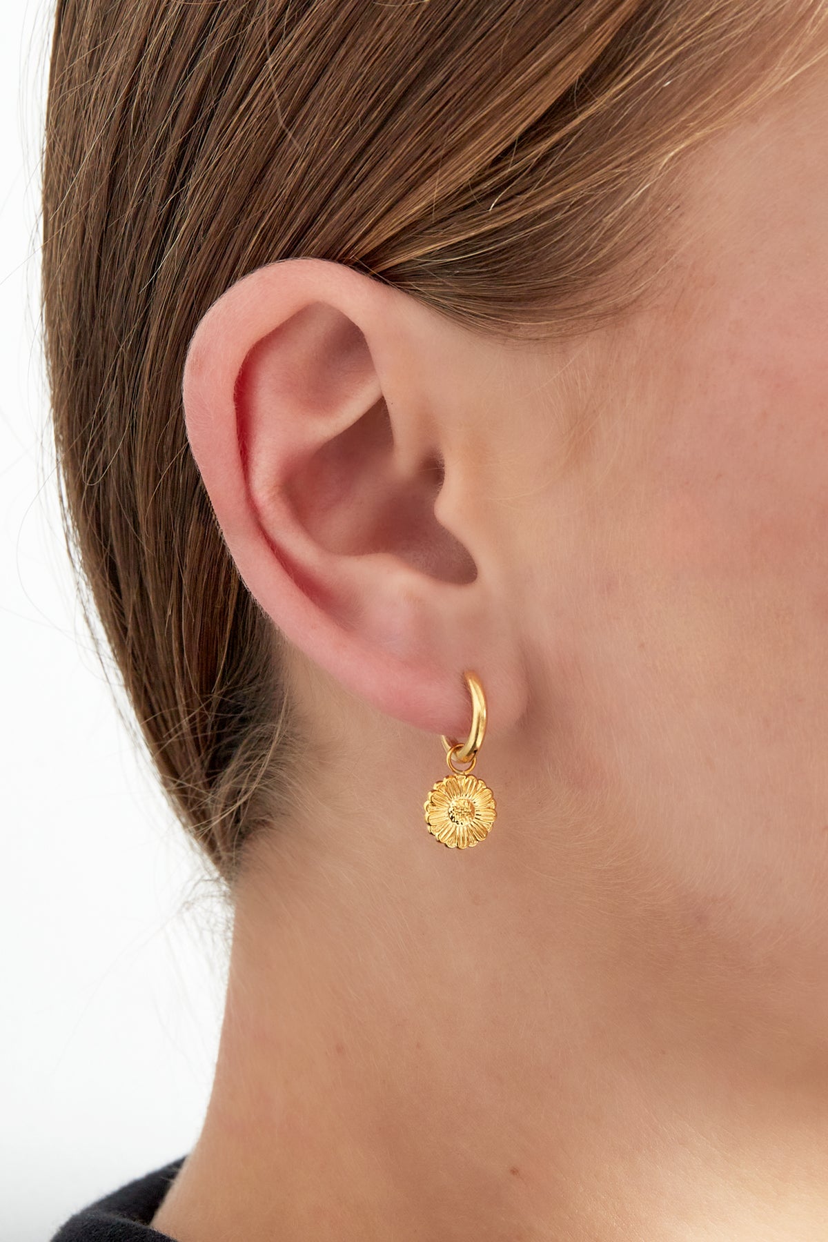 Close-up of a woman wearing a gold daisy charm hoop earring showing its playful and minimalist style