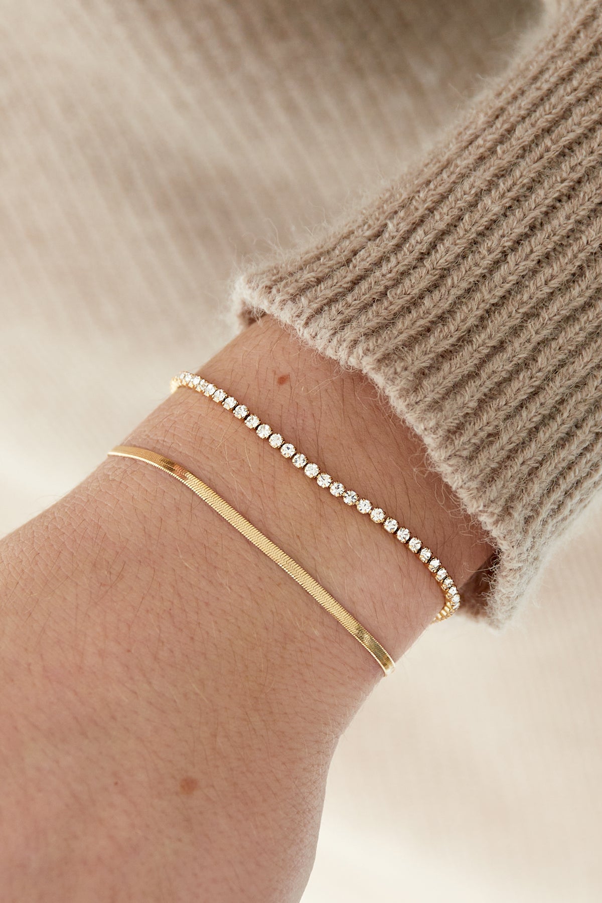 Close-up of gold tone double-layer bracelet with crystals worn on wrist with beige knit sweater