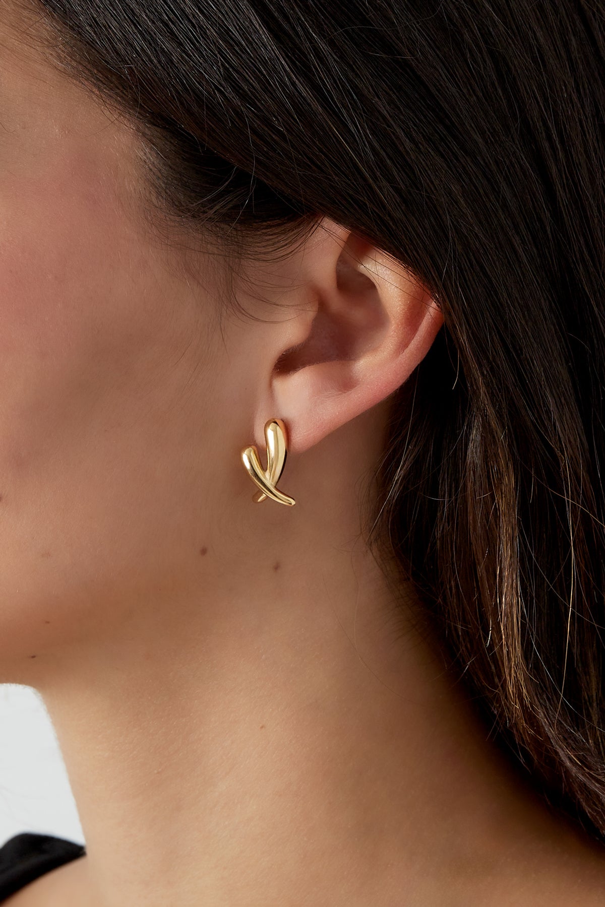 Close-up of a woman wearing gold crossed stud earrings, highlighting youthful, minimal design