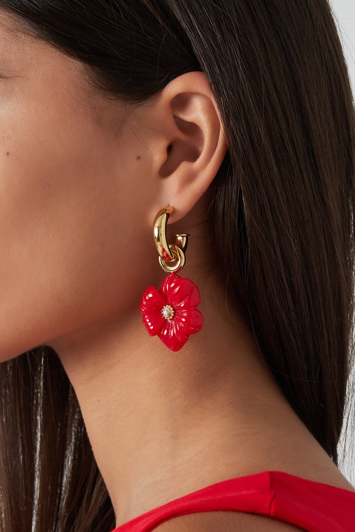 Close-up side profile of a woman wearing red flower charm gold-tone hoop earrings with a red top