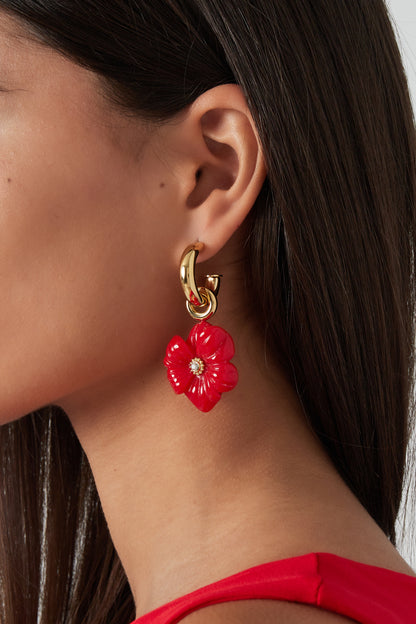 Close-up side profile of a woman wearing red flower charm gold-tone hoop earrings with a red top