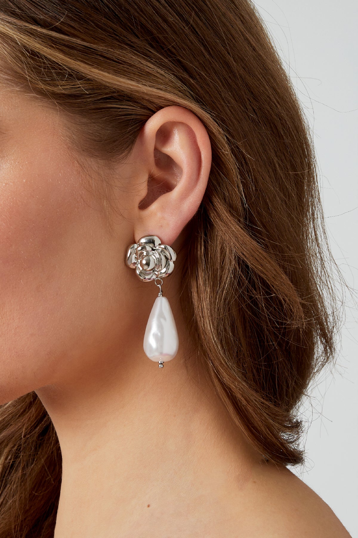 Silver rose and pearl drop earring worn on a woman's ear showcasing the size and style