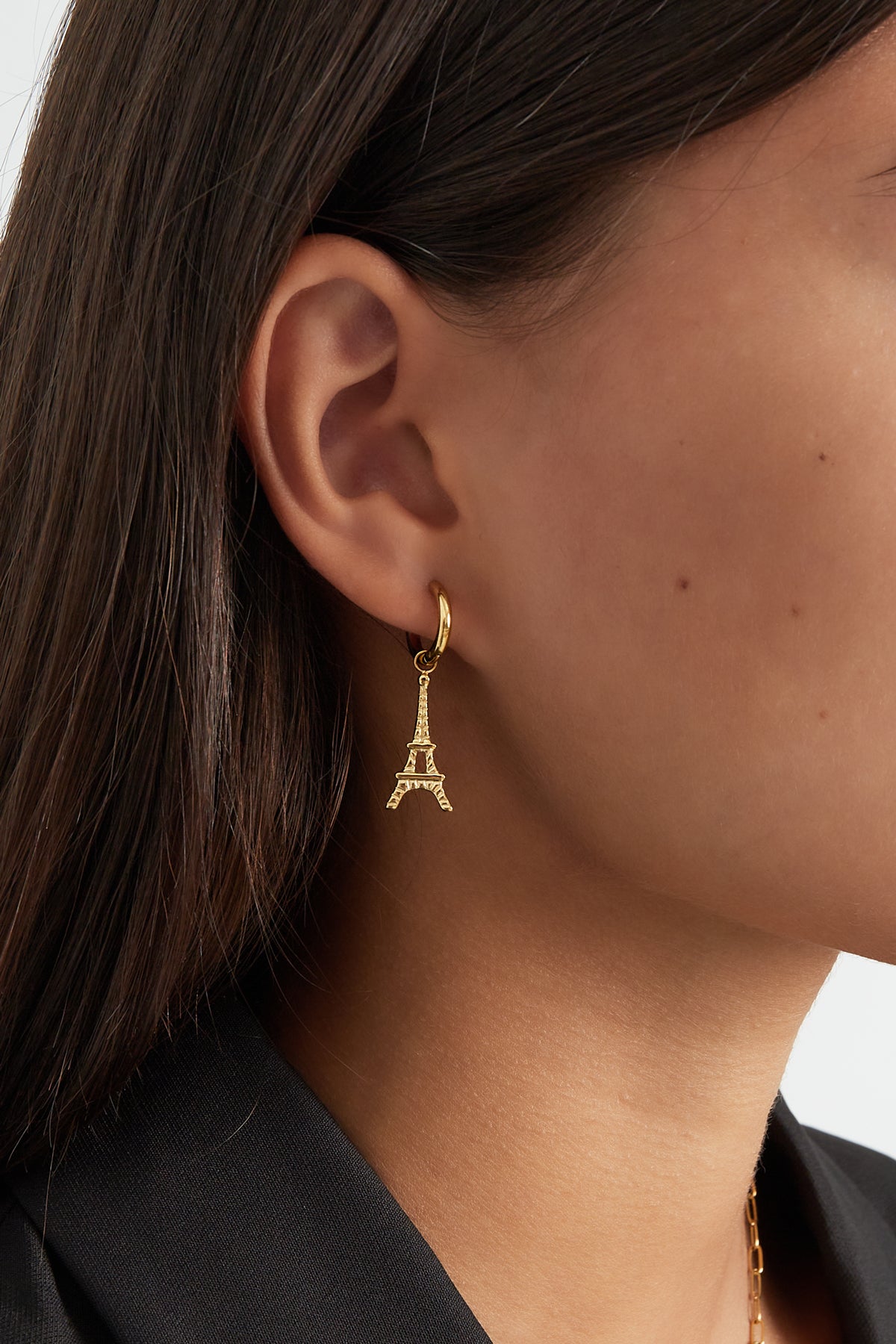 Close-up of gold Eiffel Tower drop earring worn by woman with dark hair