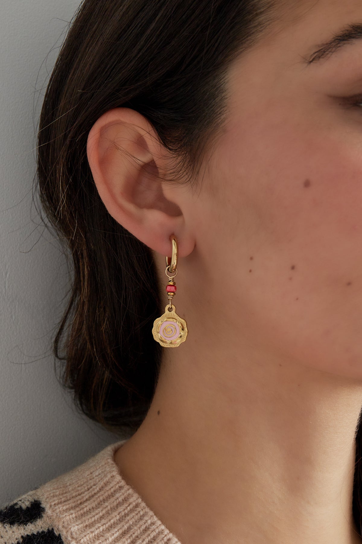 Close-up side view of a woman wearing gold-tone hoop earring with pink spiral flower and coral bead detail