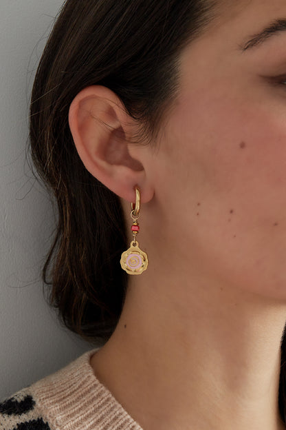Close-up side view of a woman wearing gold-tone hoop earring with pink spiral flower and coral bead detail