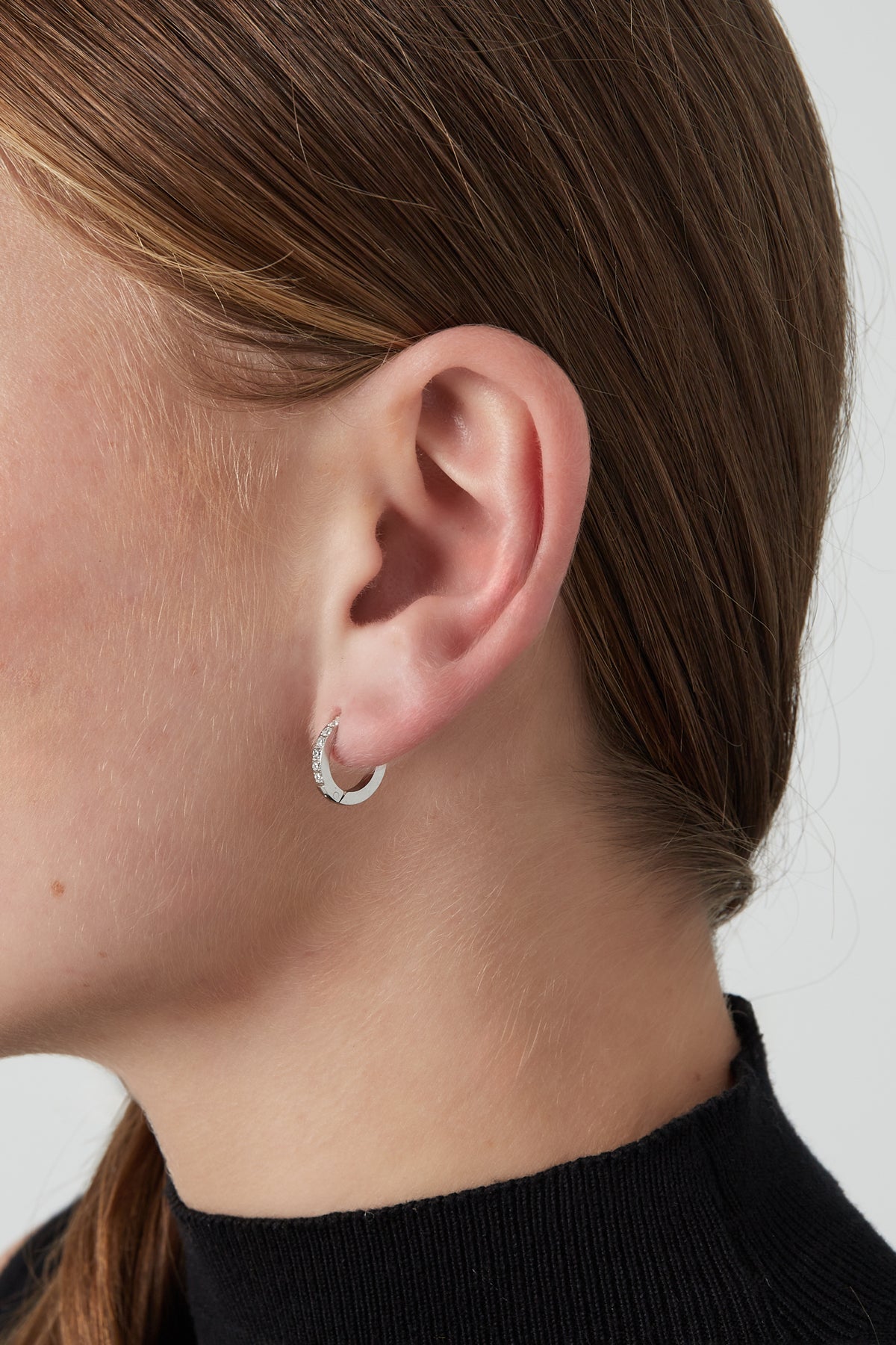 Close-up of silver mini hoop earring with clear stones worn on a woman’s ear with black top