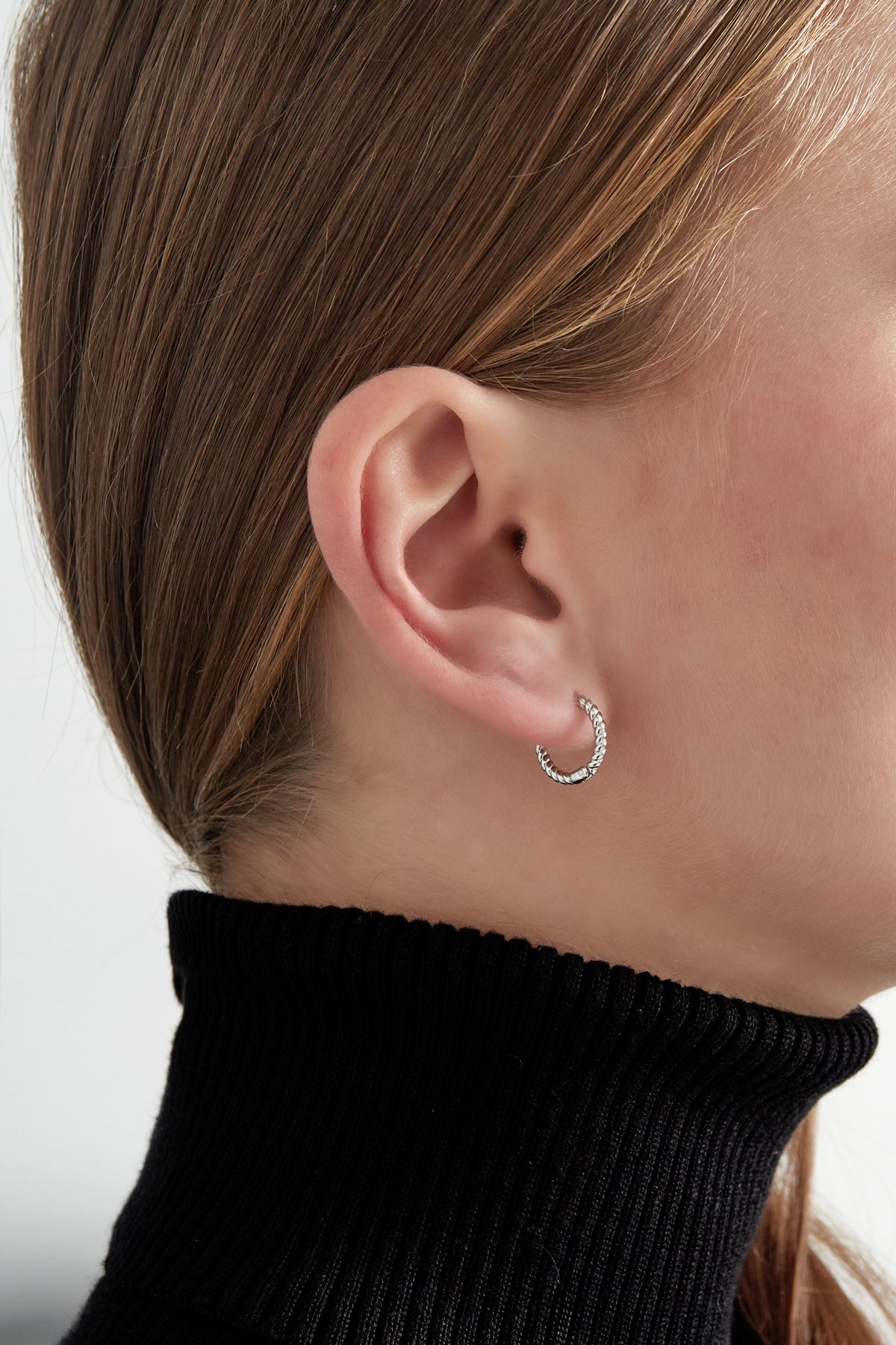 Silver twisted rope hoop earring worn on woman's ear with black turtleneck