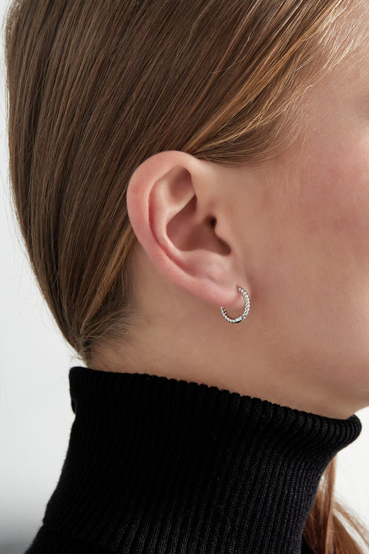 Silver twisted rope hoop earring worn on woman's ear with black turtleneck