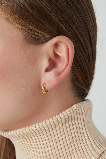 Close-up of gold mini hoop earring worn by woman with light skin and brown hair wearing cream turtleneck