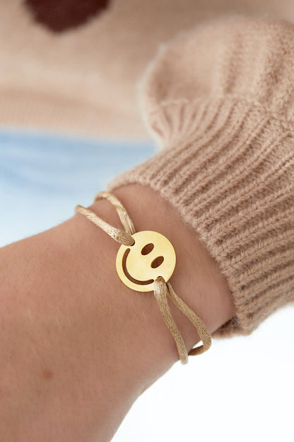 Beige satin cord smiley charm bracelet worn on wrist with beige sweater