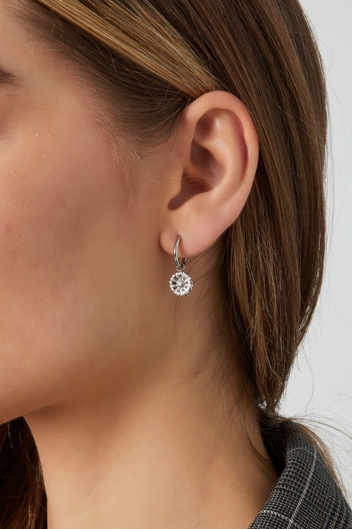 Side view of silver floral charm hoop earring worn by woman with brown hair