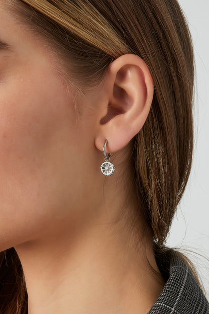 Side view of silver floral charm hoop earring worn by woman with brown hair