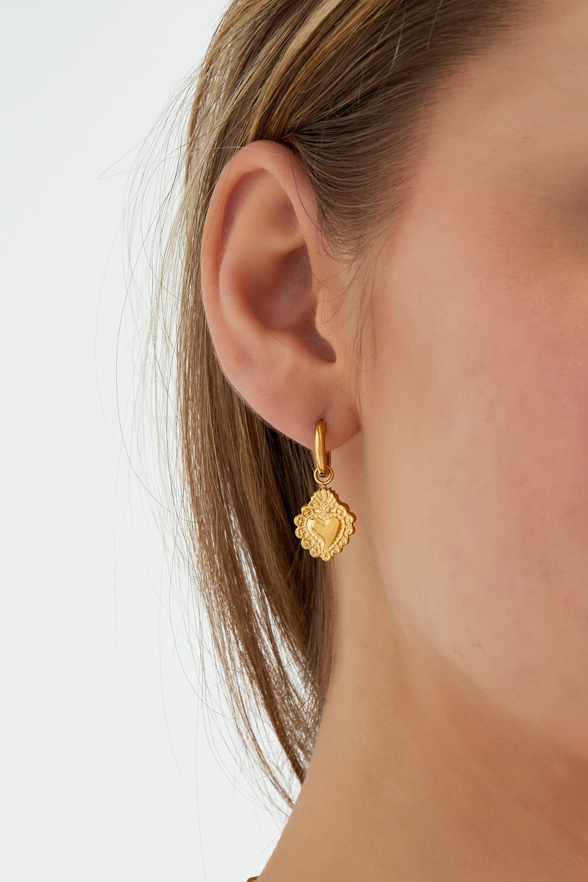 Close-up of gold heart charm hoop earring worn on a woman's ear, showing youthful and minimal style