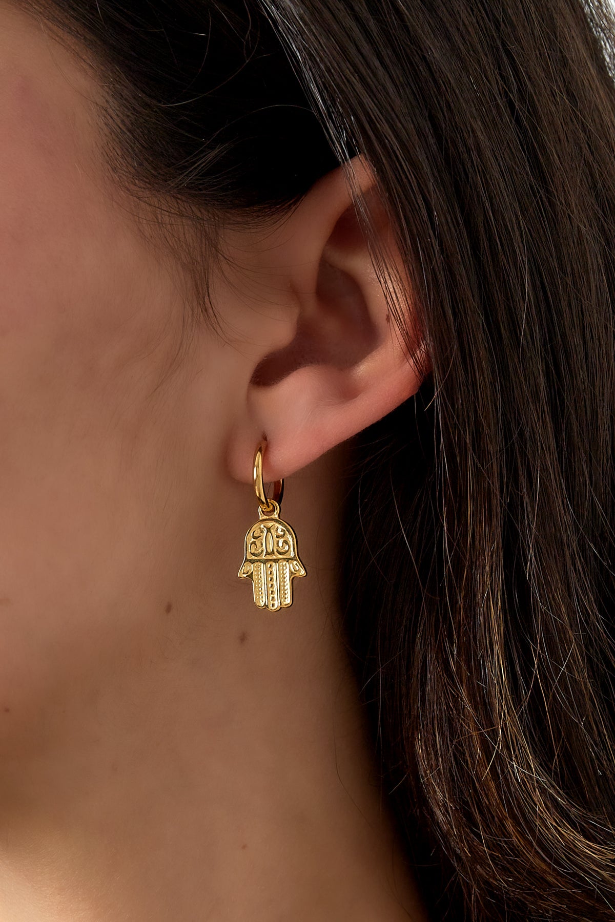 Close-up of woman wearing gold tone Hamsa charm hoop earring on ear