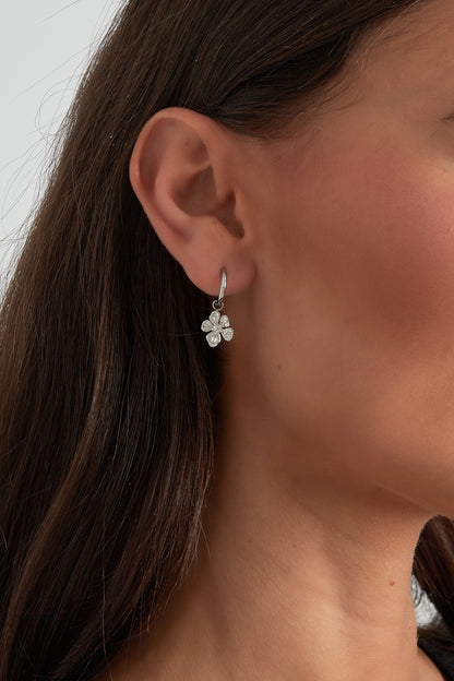 Close-up of a woman wearing silver hoop earrings with a delicate flower charm