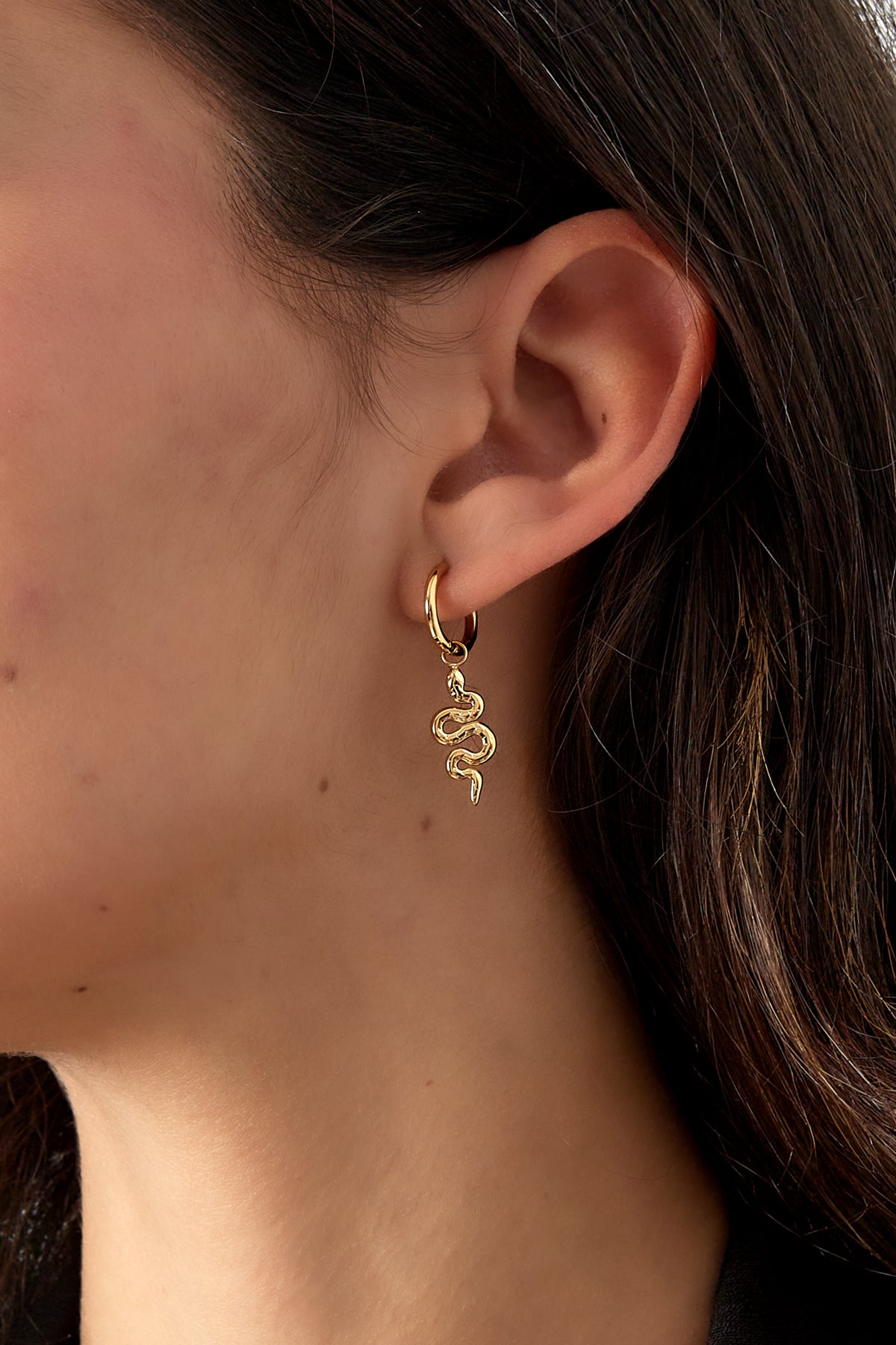 Close-up of gold snake charm hoop earring worn on a woman's ear with dark hair