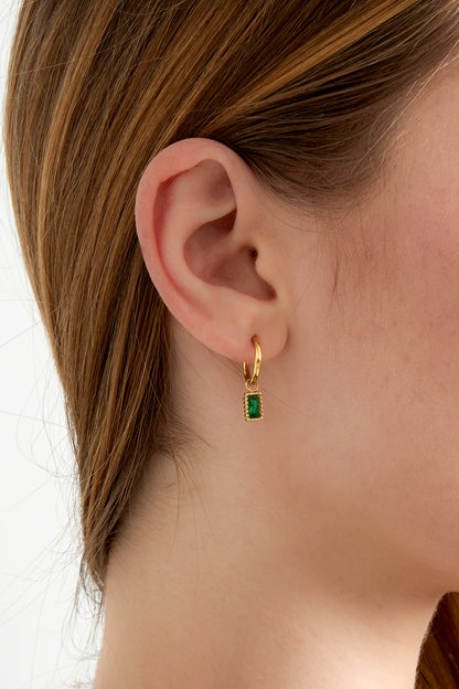 Close-up of woman wearing gold hoop earrings with green rectangular gemstone charms