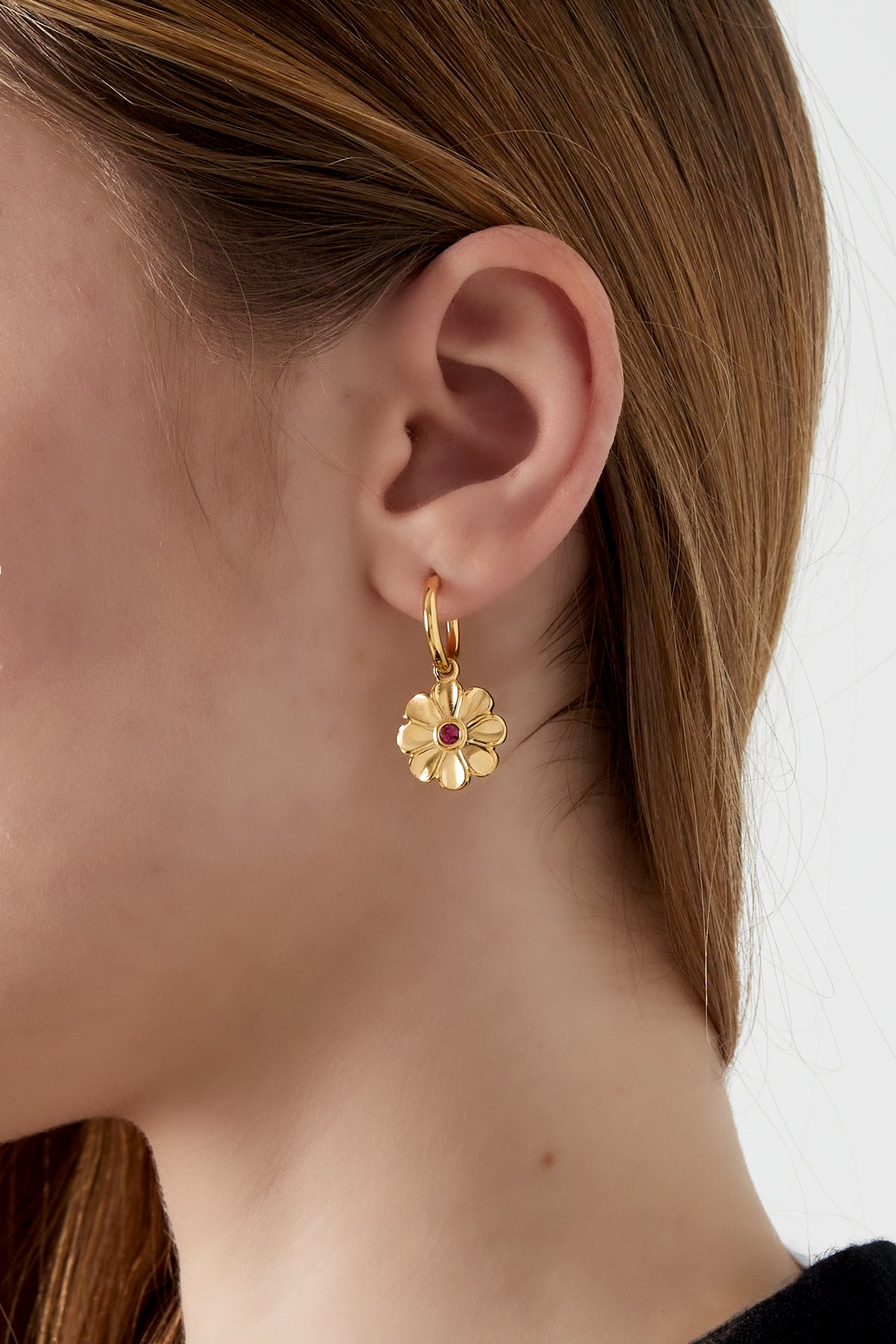 Close-up of a woman wearing a gold-tone floral charm hoop earring showing soft youthful style