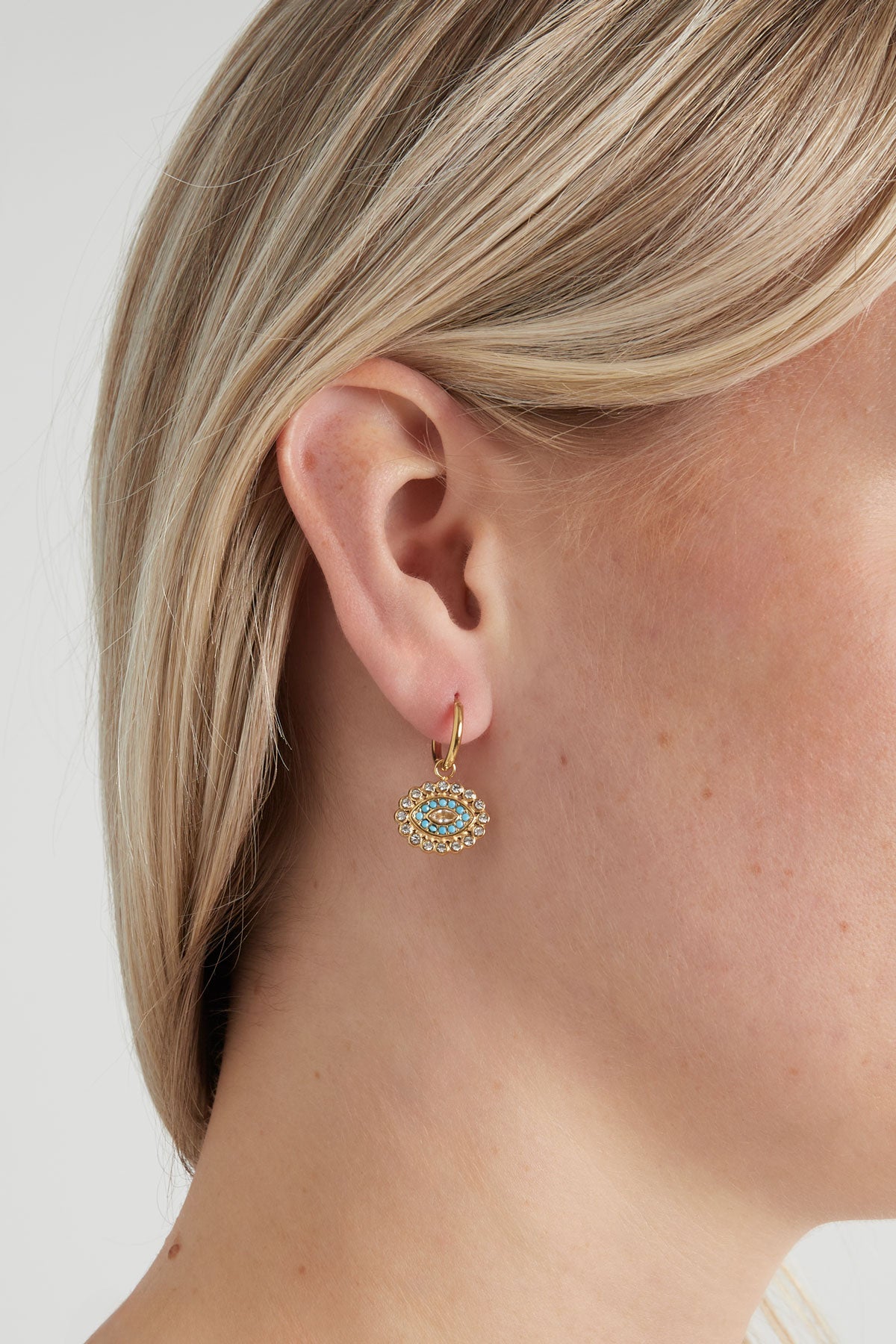 Close-up of woman wearing gold hoop earrings with evil eye charm featuring turquoise beads and rhinestones