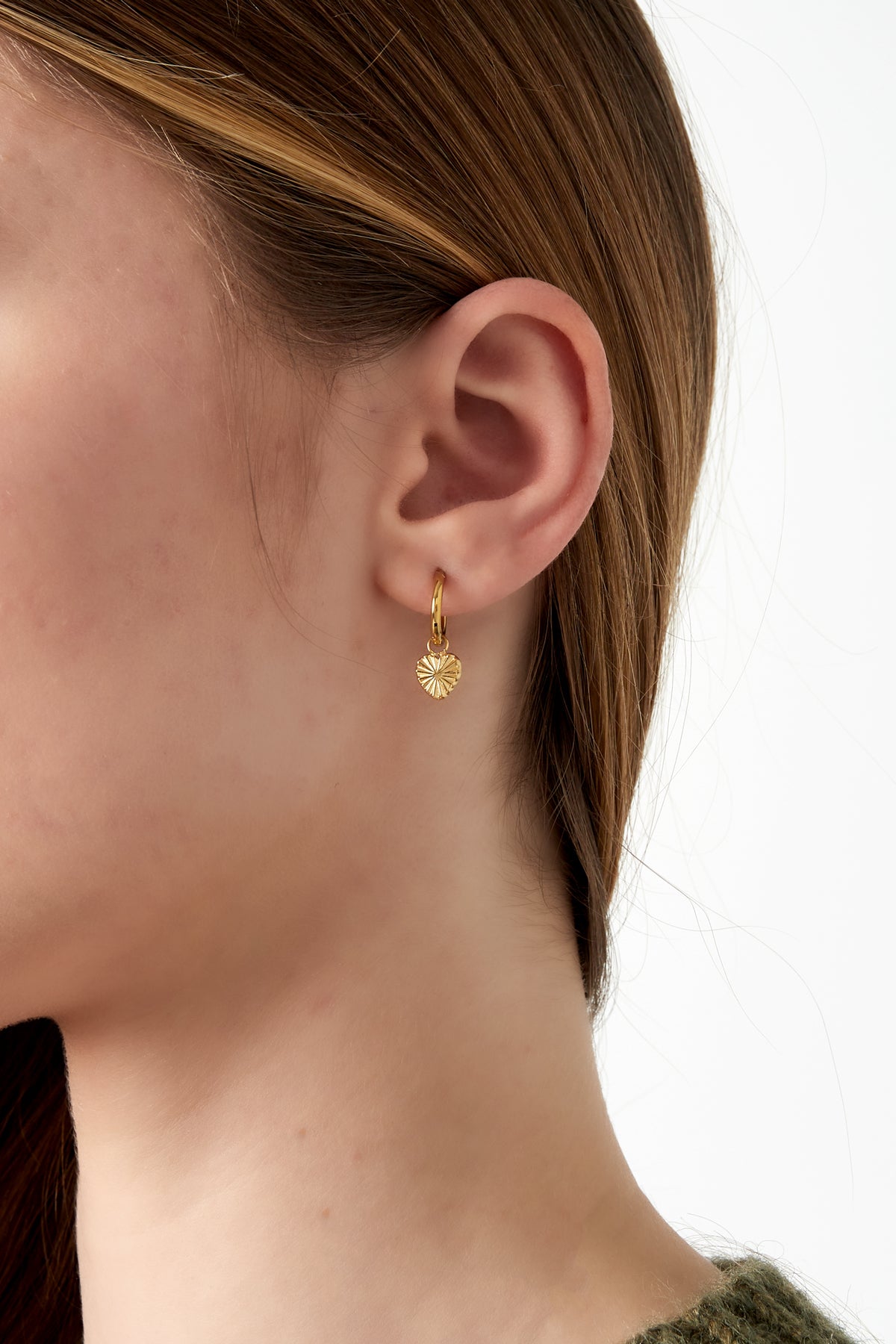 Close-up of a woman's ear adorned with a gold hoop earring with a sunburst heart charm