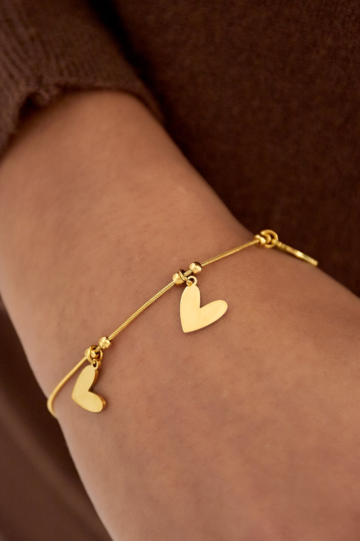 Close-up of gold heart charm bracelet worn on wrist with brown sweater background