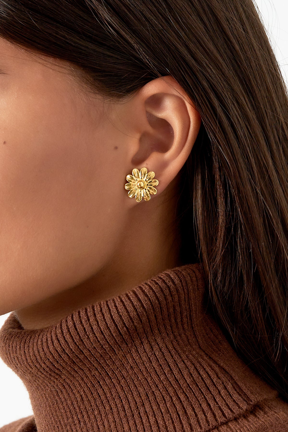 Close-up of a woman wearing a gold daisy stud earring paired with a brown turtleneck sweater