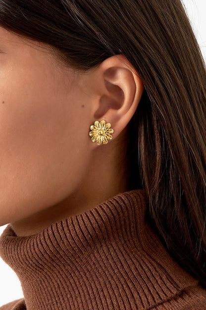 Close-up of a woman wearing a gold daisy stud earring paired with a brown turtleneck sweater